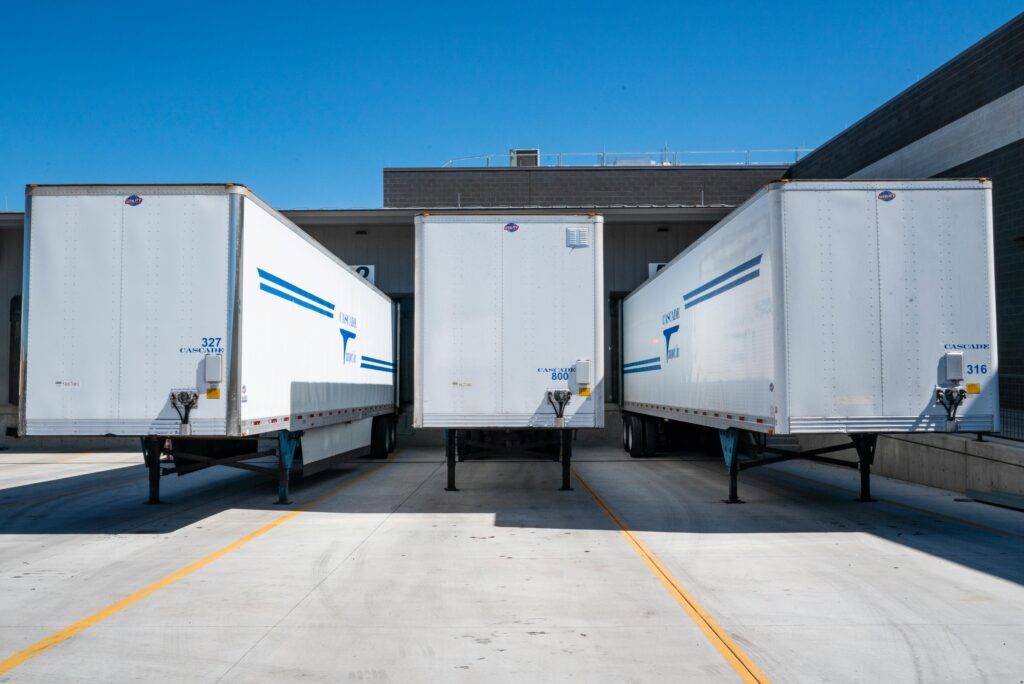 pexels-photo-1267325-1267325 Three white cargo trailers parked at an industrial shipping dock under clear blue skies.